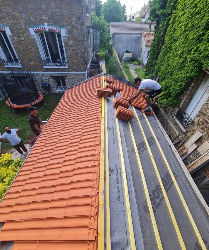 Couvreur en train de poser des tuiles neuves sur un écran sous-toiture et des liteaux